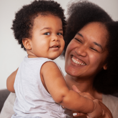 Mother smiling while holding her baby daughter, representing dental care for infants in wilmington nc