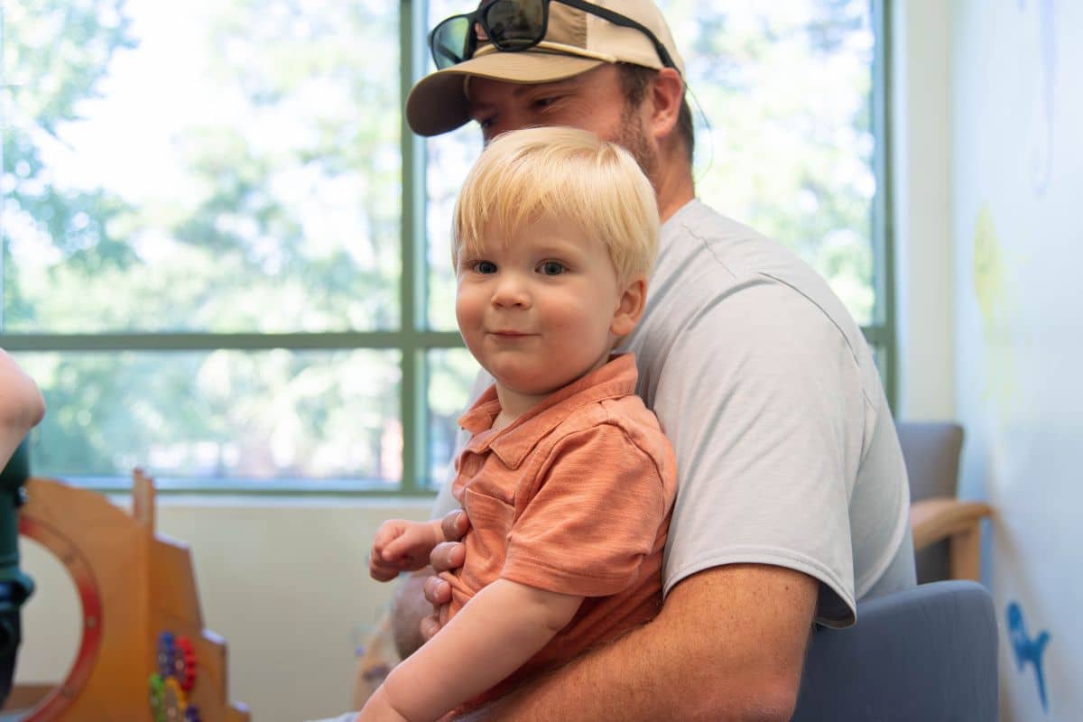Little boy smiling in his dad’s arms in the Wilmington Pediatric Dentistry waiting room before sealant treatment